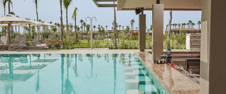 Entspannte Stunden am türkisblauen Pool des 4-Sterne Lusso Sorgun, umgeben von Palmen und grünem Umfeld unter klarem, sonnigem Himmel.